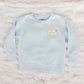 Light blue sweatshirt with a small logo on a textured white surface