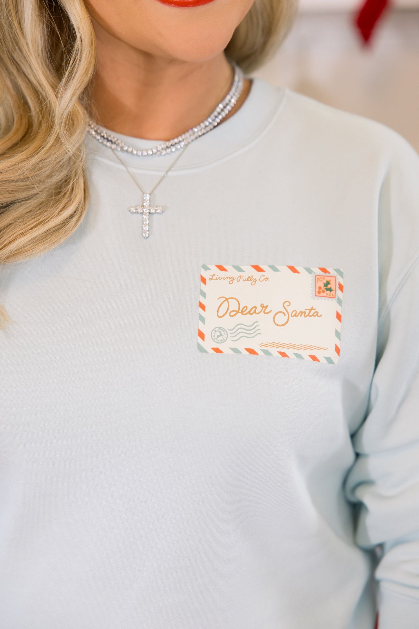 Light blue sweatshirt with a 'Dear Santa' postcard printed patch worn by a person.