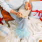 Person sitting on a chair with a gift bag and wrapped presents in a festive setting.