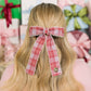 Person with a red plaid hair bow in front of gift boxes