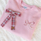 Pink sweatshirt with plaid bow and embroidered bow on a white textured background