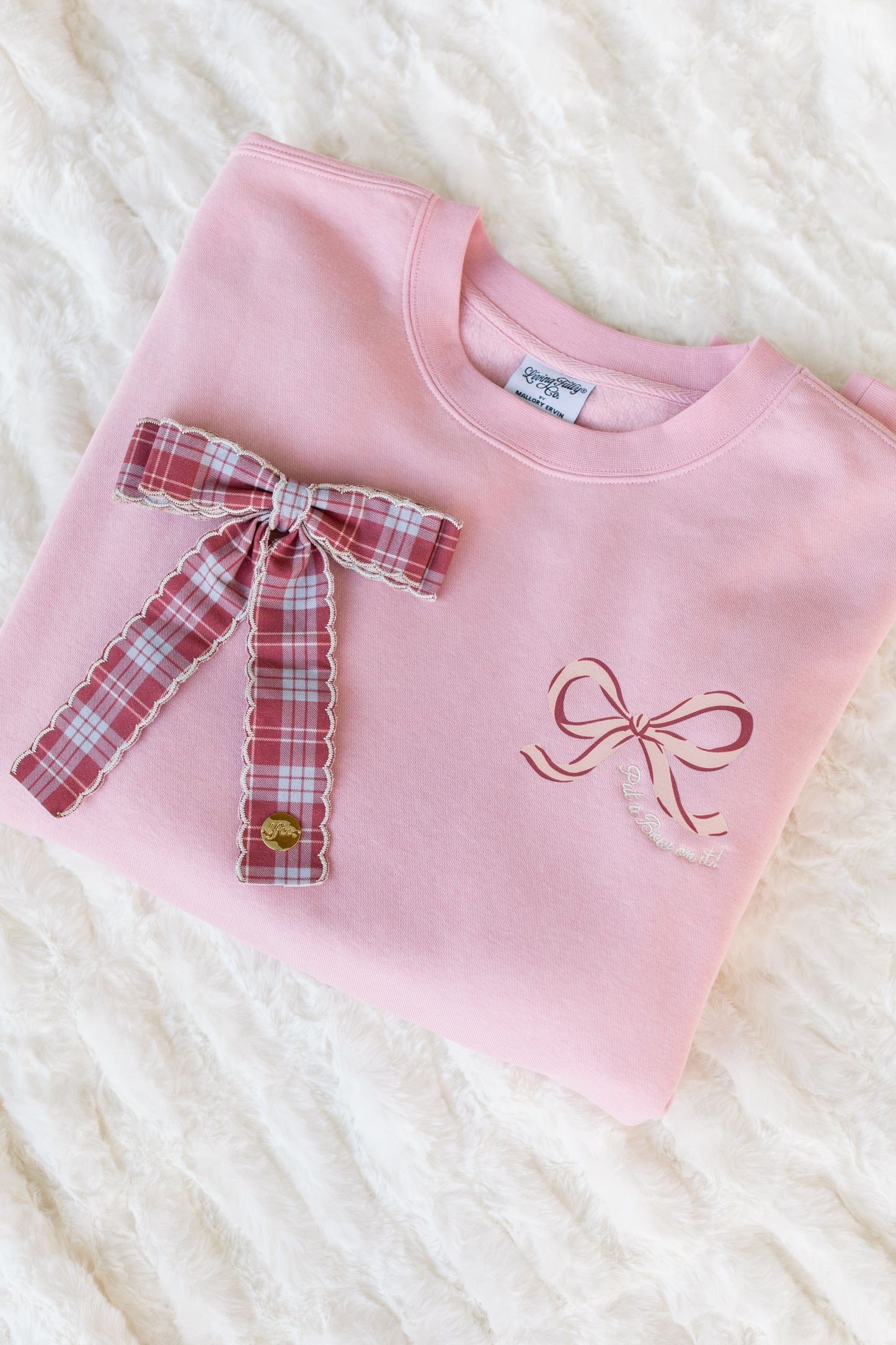 Pink sweatshirt with plaid bow and embroidered bow on a white textured background