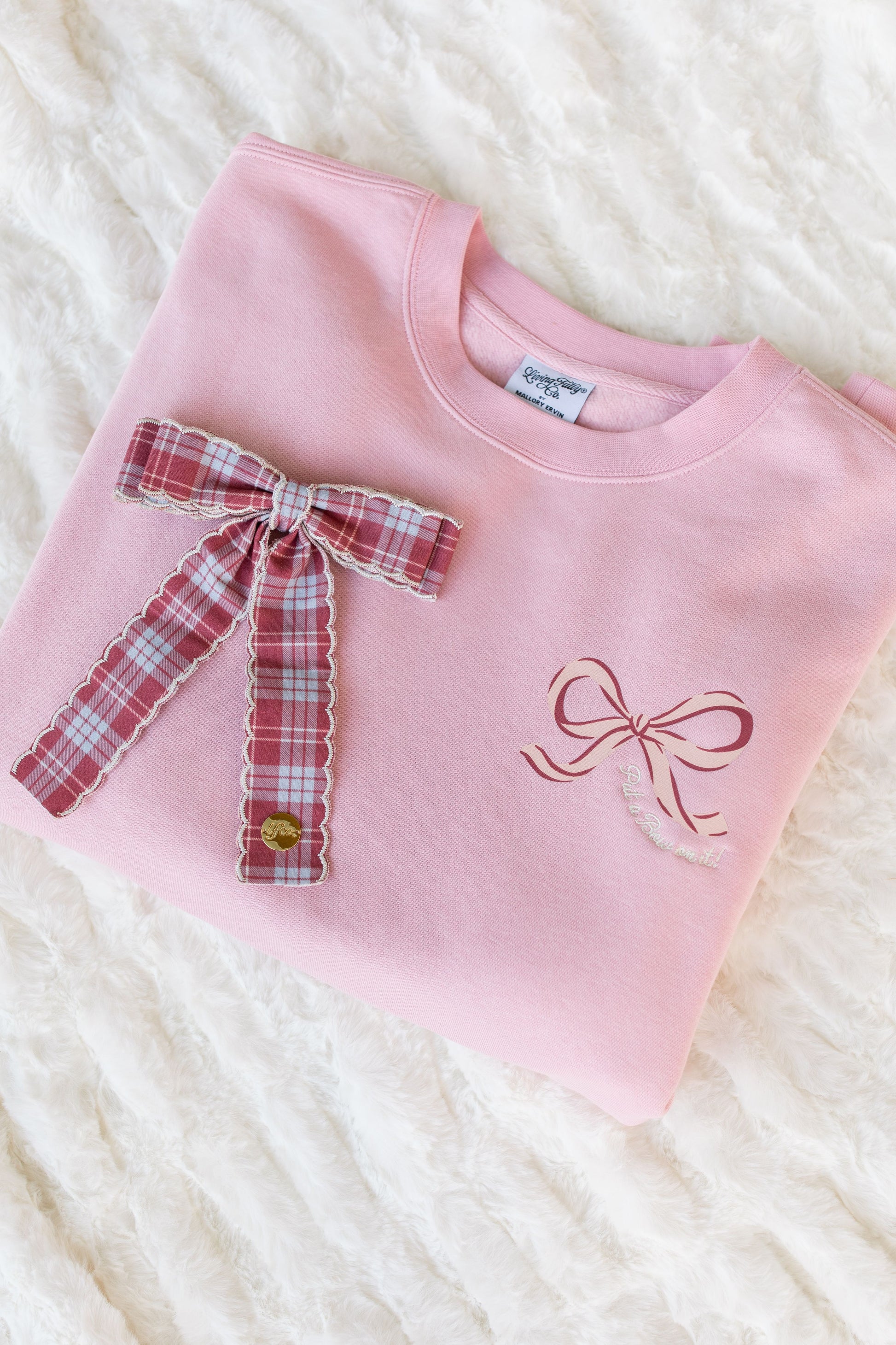 Pink sweatshirt with plaid bow and embroidered bow on a white textured background