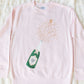 Pink long-sleeve shirt with champagne bottle graphic and text on a textured white background
