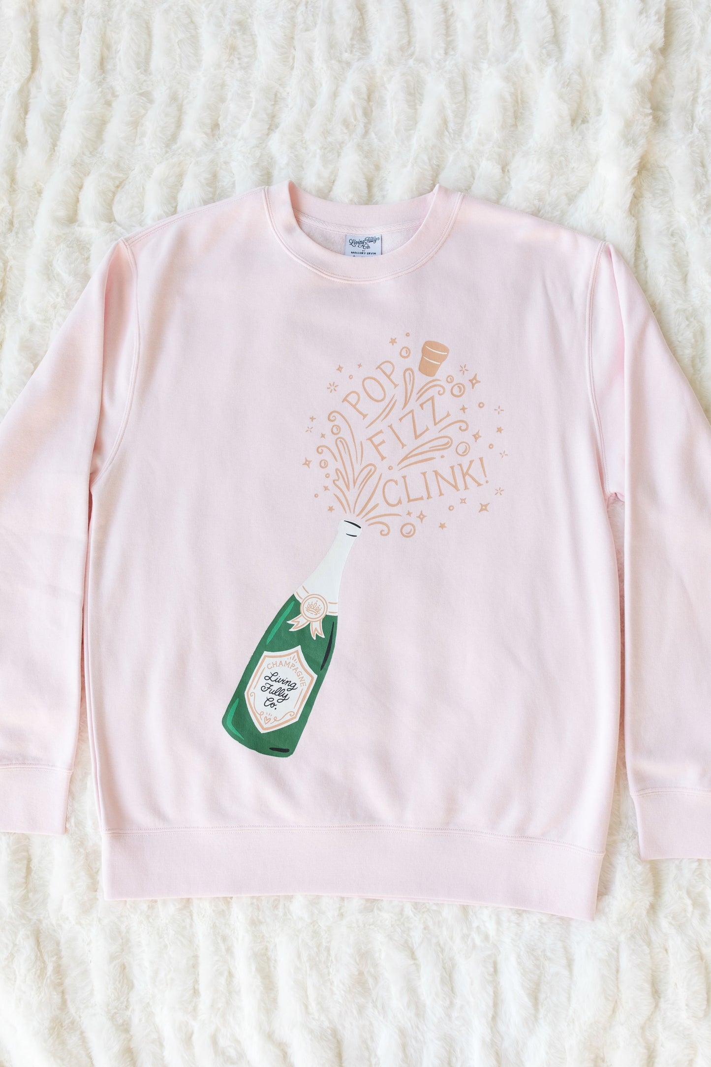 Pink long-sleeve shirt with champagne bottle graphic and text on a textured white background