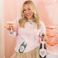 Woman holding a bottle of champagne and a cocktail in a celebratory setting with pink balloons.
