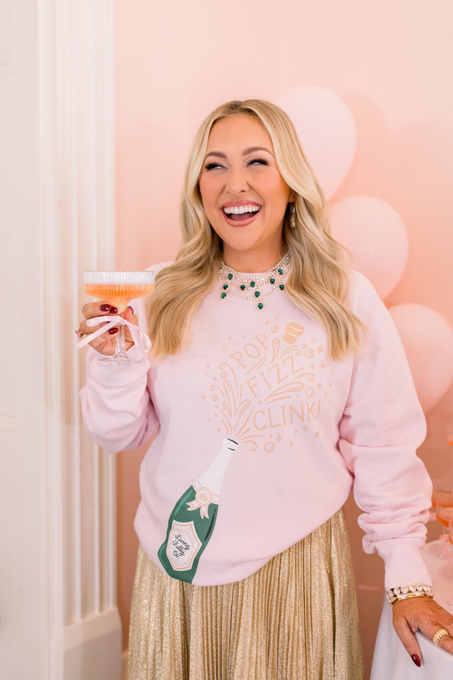 Woman in a pink sweatshirt with a drink and bottle against a light pink background
