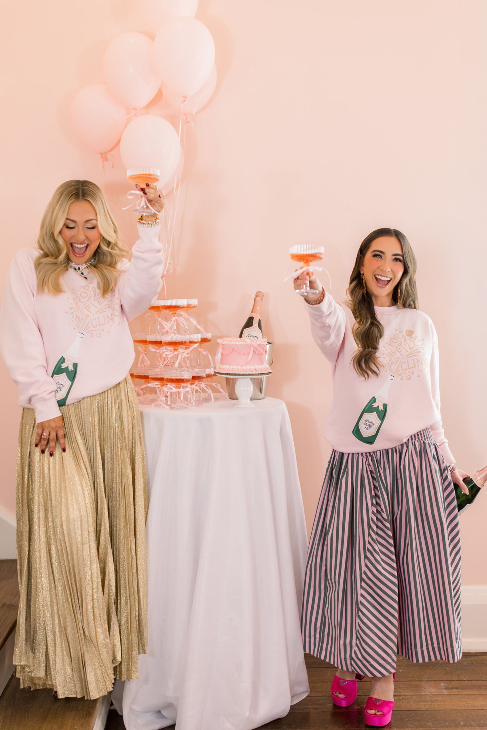 Two women in matching sweaters with a cake and balloons in the background