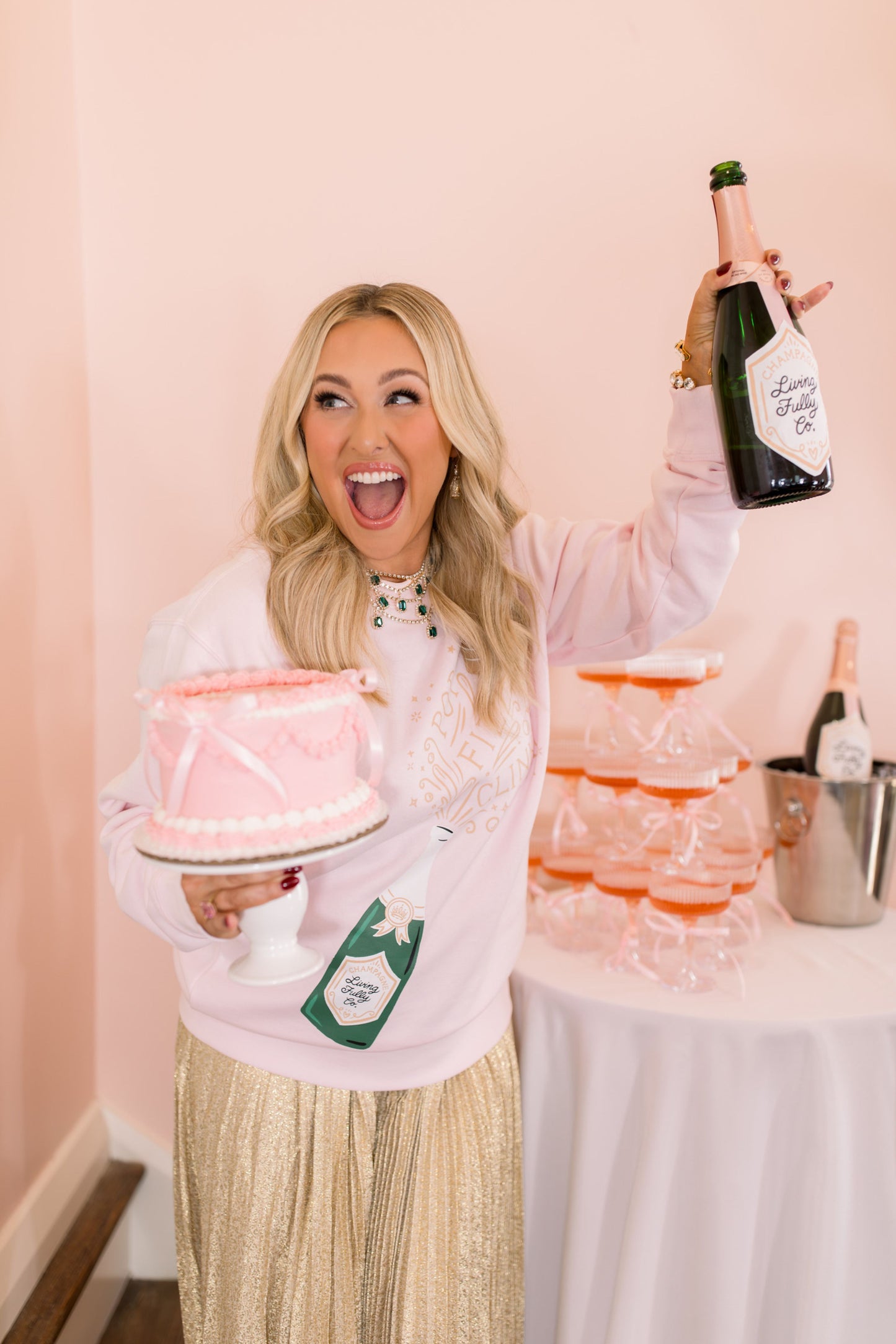Woman holding a cake and a bottle of champagne in a celebratory setting.