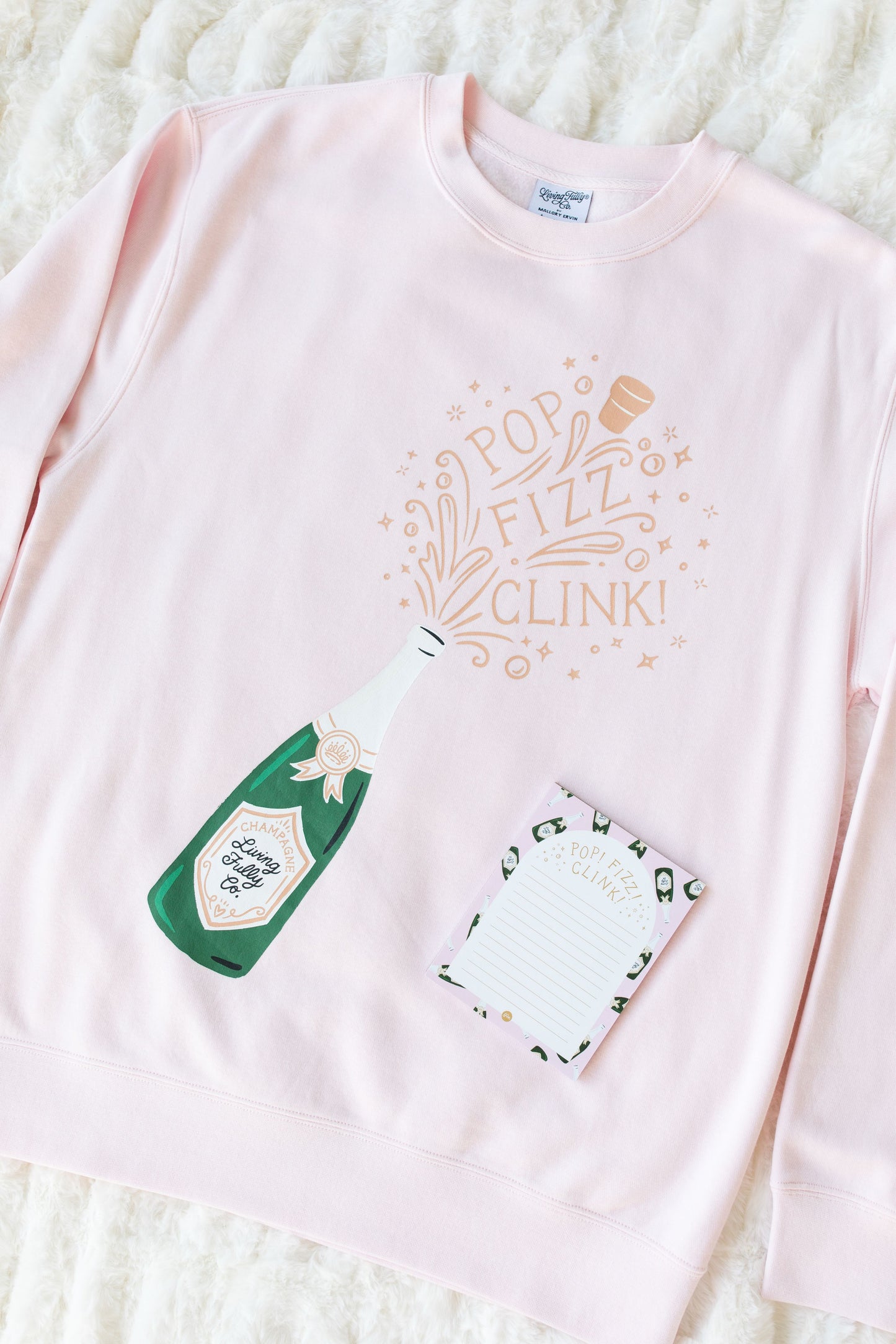 Pink sweatshirt with 'Pop Fizz Clink!' design on a textured white background