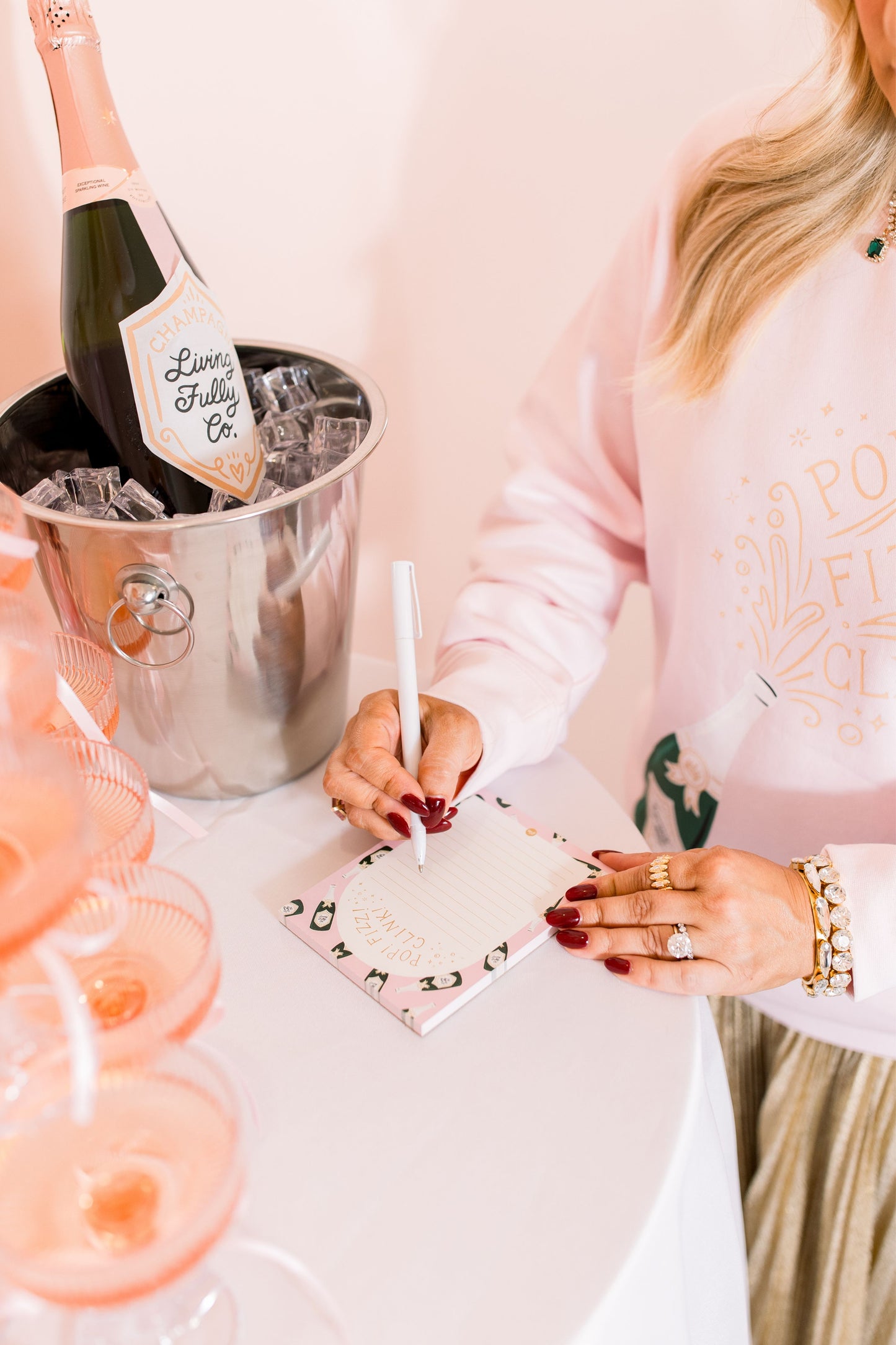 Person writing on a notepad with a bottle of champagne in the background