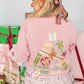 Person wearing a pink sweater with festive designs in a gift-wrapping setting