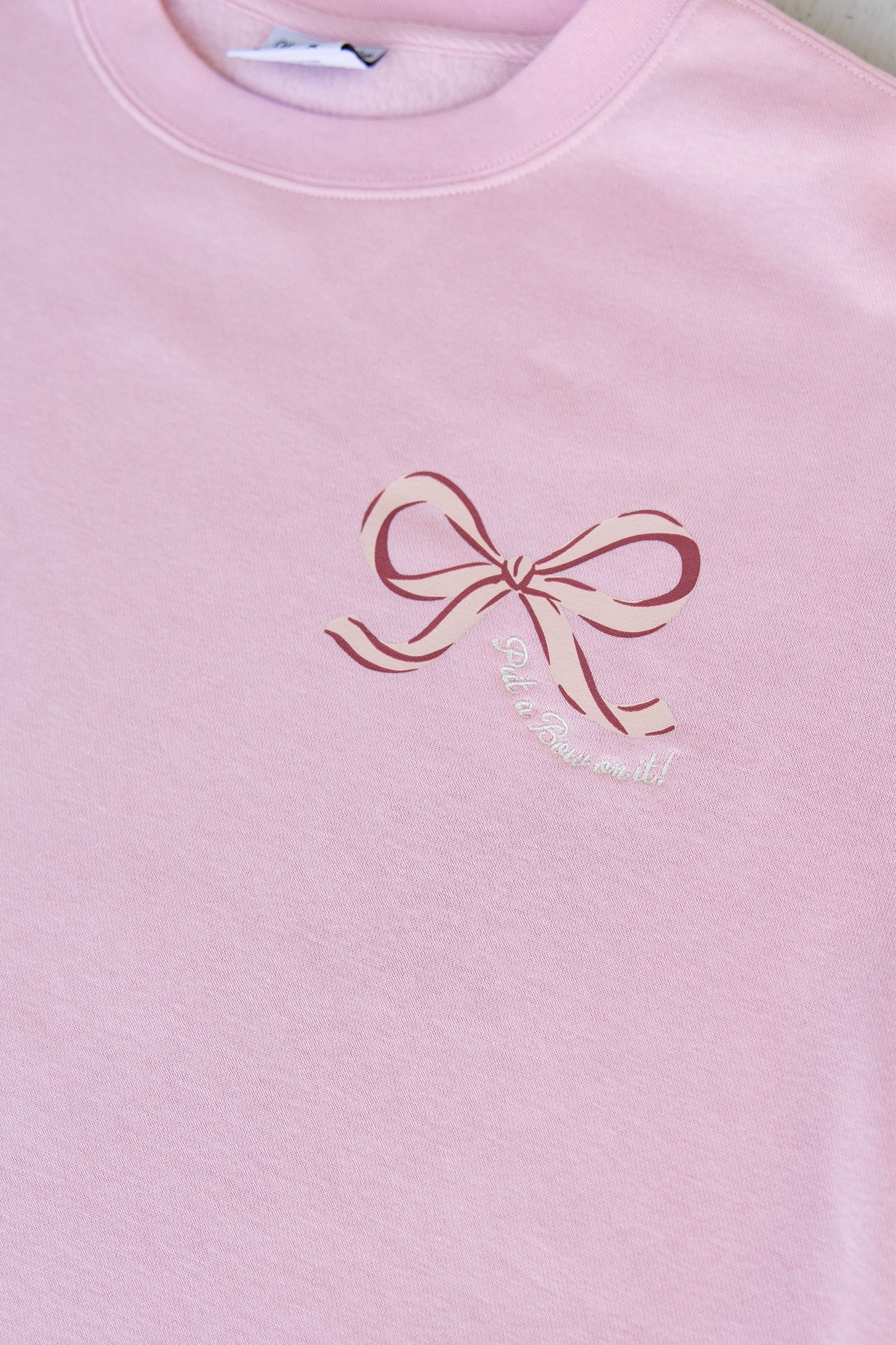Pink sweatshirt with a bow design and text on a plain background