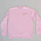 Pink sweatshirt with a logo on a light gray wooden surface
