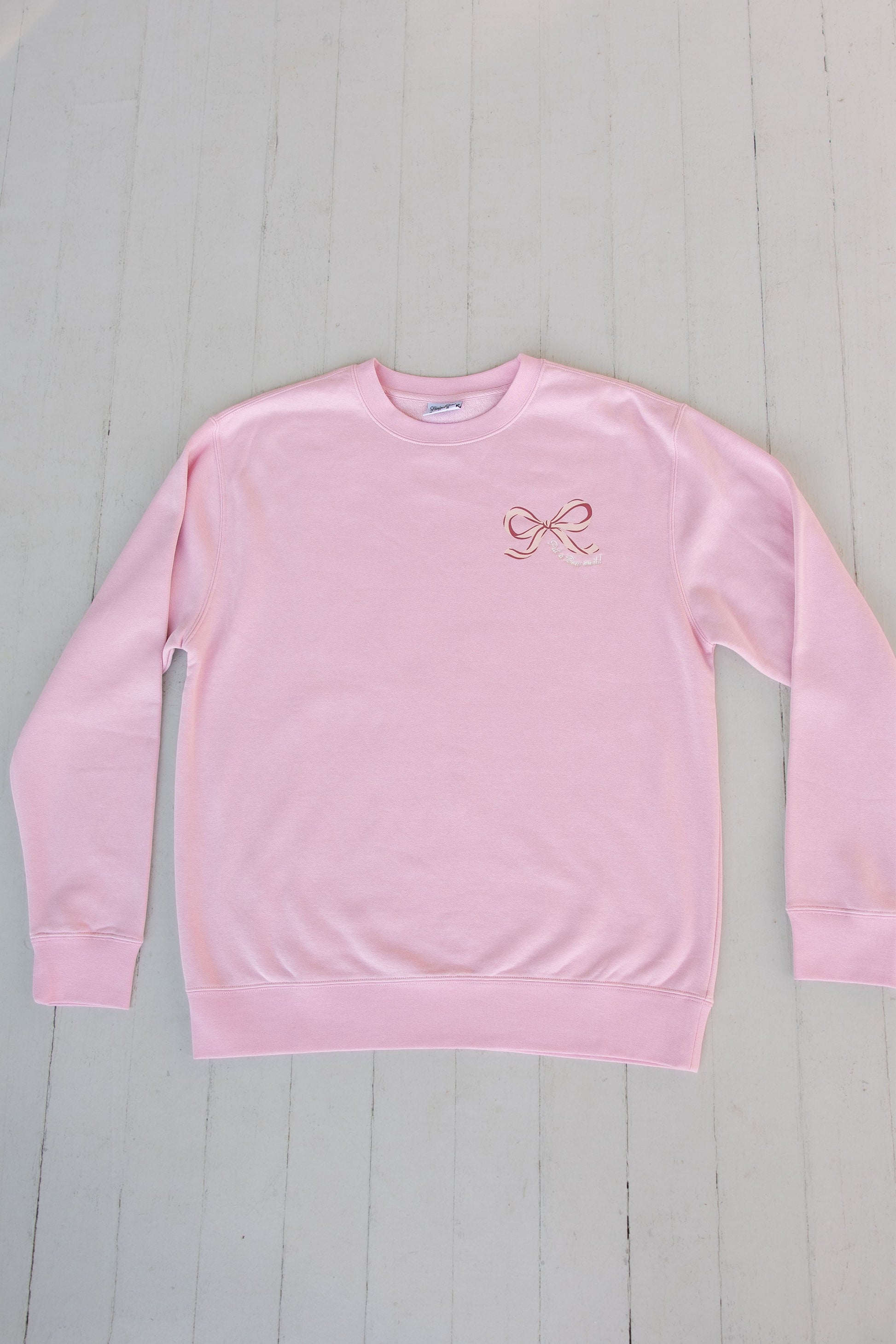 Pink sweatshirt with a logo on a light gray wooden surface